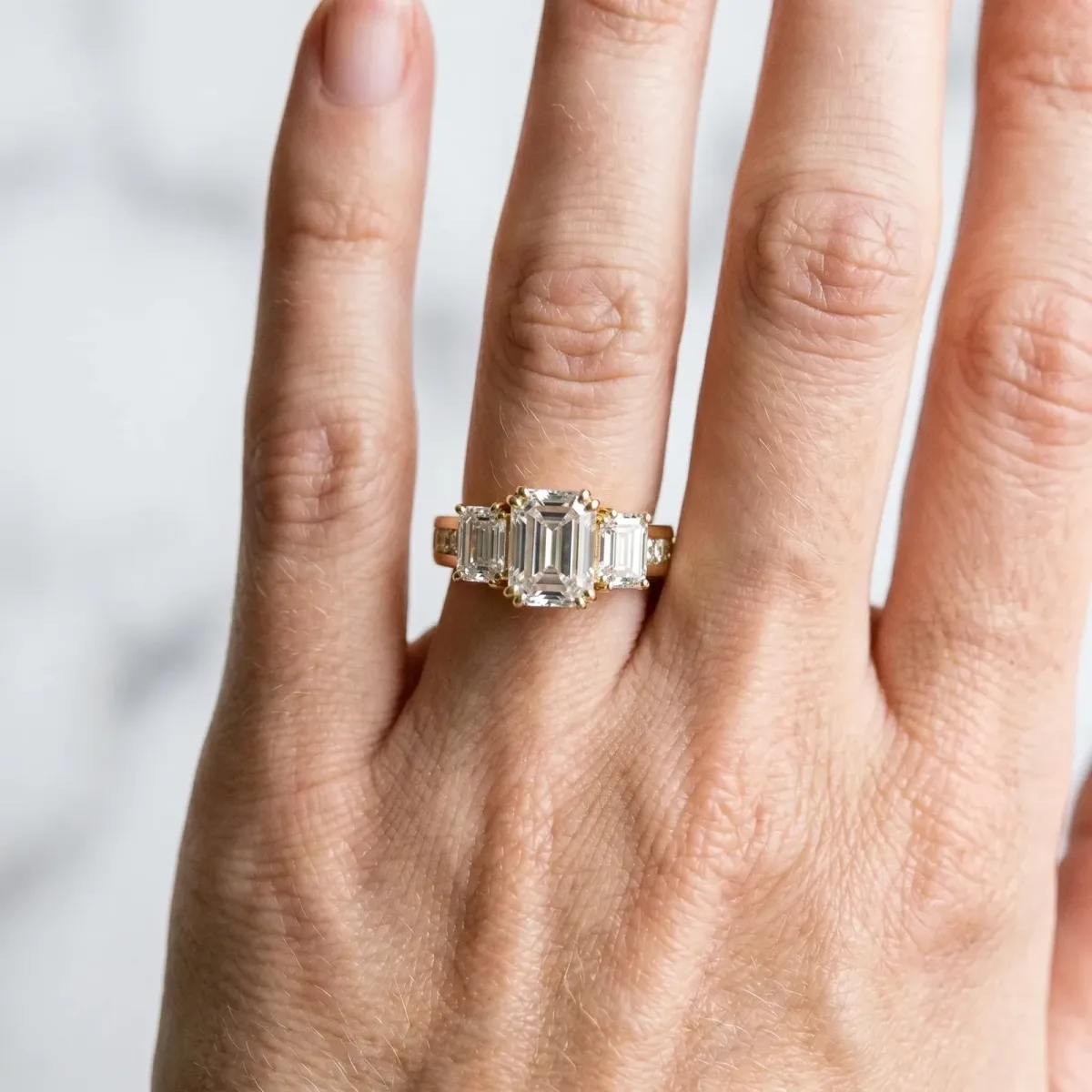 Three-Stone Emerald Cut Cut Diamond Ring with Channel Set Band and Four-Prong Setting Yellow gold